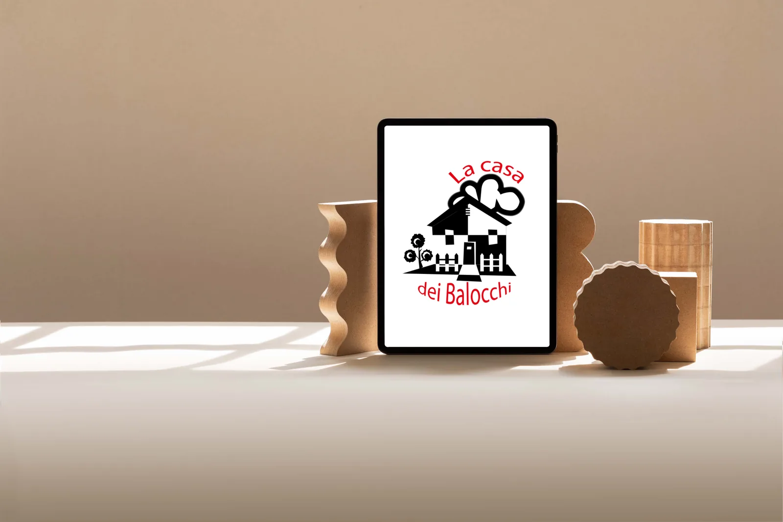 Creazione visual e brand identity: il logo La Casa dei Balocchi su un tablet, appoggiato tra forme di legno chiaro