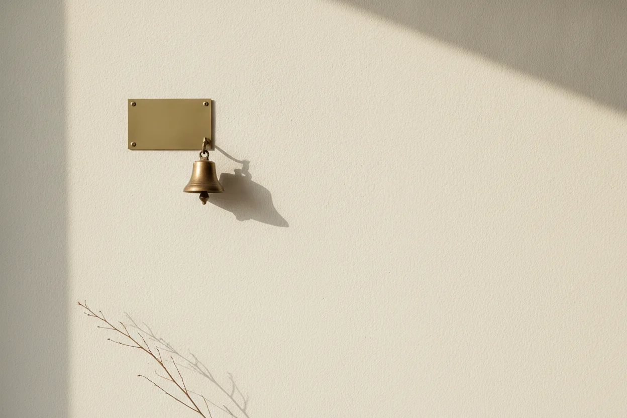Come trovare clienti online: una targa d'ottone senza nome e un campanello di bronzo su un muro crema